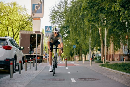 Man bicyclist wearing sportive clothing, sunglasses and protective helmet riding fast to place of training destination using city bicycle path
