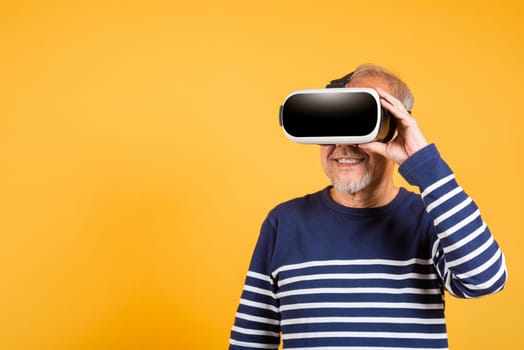 Portrait Asian smiling old man holding in a virtual reality glasses headset studio shot isolated yellow background, Excited happy senior man pensioner using VR play simulation game