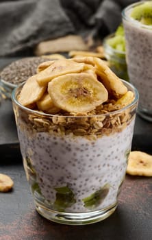 Glass of chia seed pudding layered with kiwi, topped with granola and banana chips