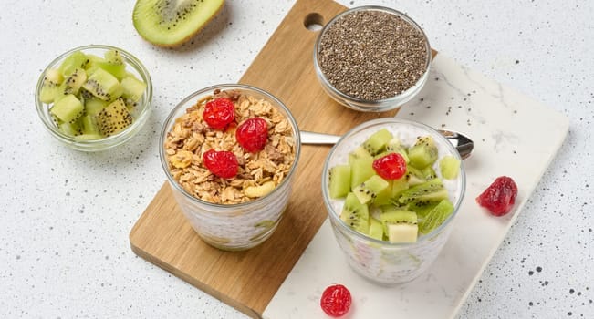 Yogurt and chia seed pudding in a glass, kiwi pieces. White table, top view