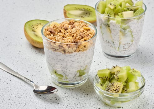 Glass filled with chia seed pudding, layered with diced kiwi at the bottom and topped with crunchy granola
