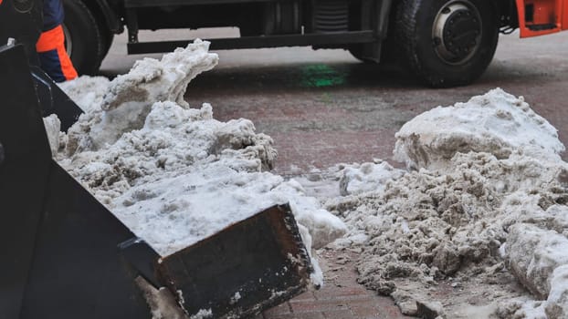 Tractor shovel loading snow and ice into a truck during snow removal in winter