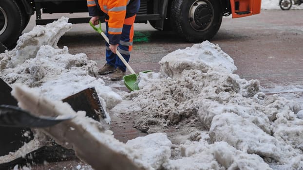 Road worker cleaning street from snow with a shovel next to a truck after heavy snowfall