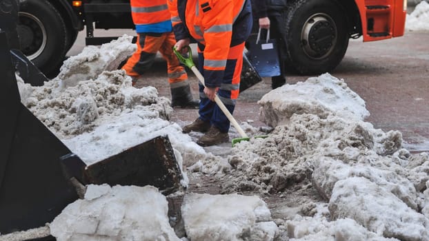 Road workers cleaning city street from snow with shovels and truck in winter