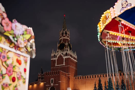 Spasskaya Tower of Moscow Kremlin illuminated at night with christmas market attractions and carousel lights in winter