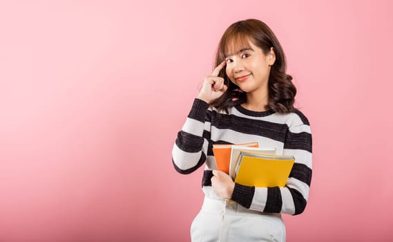 Portrait of beautiful Asian young woman teenage smiling hugging books, female person holding book and thinking idea, studio shot isolated on pink background with copy space, education concept