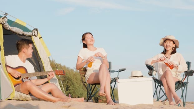Happy friends with drinks in camp and laughing together in holidays on sand beach near camping tent vacation time at sunset, Young Asian group woman and man in summer travel outdoor