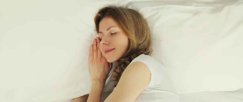Happy young woman sleeping lying in bed on white soft comfortable pillow in bedroom at home, copy space background