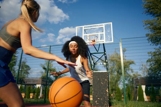 Athlete girls playing basketball game together at outdoor court during sunny summer day. Active leisure time concept