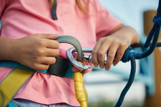 Getting ready for adventure in rope park. Closeup view on protective gears for climbing in hand of little girl child. Safety and risk