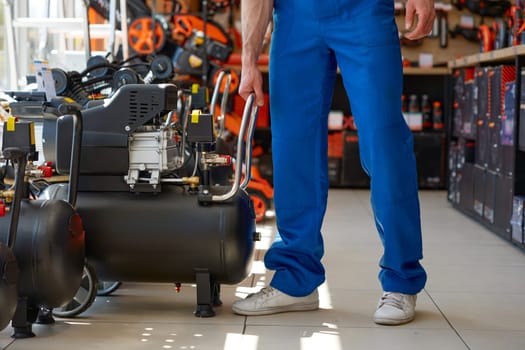 Crop of workman in overalls choosing compressor at hardware store. Man buying equipment to supply of compressed air or gas to pneumatic tools for trouble-free operation