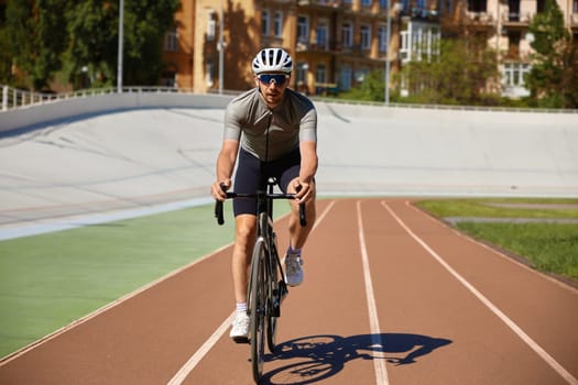Bicyclist wearing sports clothing and protective helmet cycling on velodrome. Young sportsman exercising preparing for competition or marathon on track. Hobby and active lifestyle concept