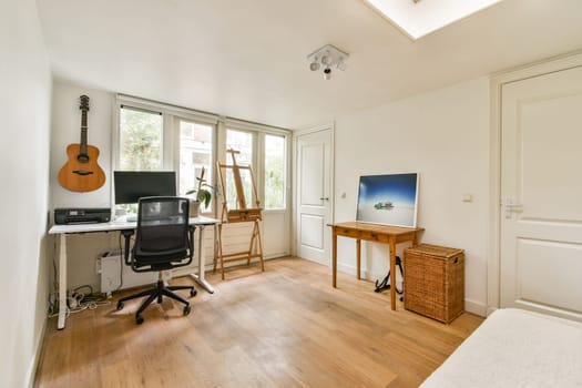 A clean and bright home office featuring a desk with a computer, acoustic guitar, and natural light from large windows. A perfect blend of functionality and style.