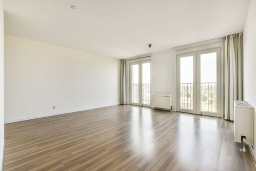 Bright and spacious apartment interior featuring wooden flooring, large windows, and a simple, uncluttered design for a serene living environment.