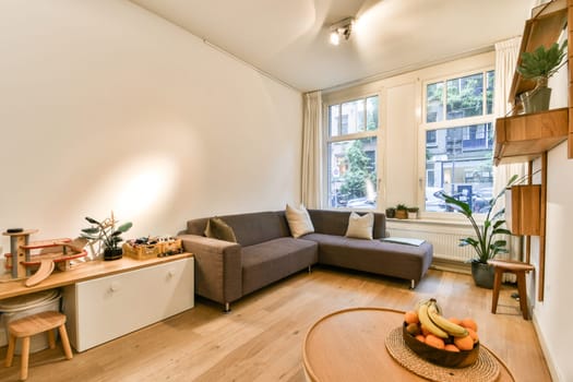 A stylish and cozy modern living room featuring a gray sofa, wooden furniture, and bright natural light flooding through the windows, creating an inviting atmosphere.