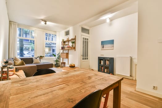The image showcases a bright, cozy modern interior featuring a wooden table, comfortable seating, and natural light streaming through large windows.