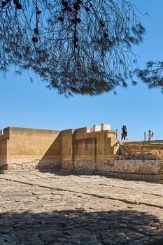 Crete.Greece - april 24, 2025: The photograph showcases the archaeological site of Knossos, displaying stone walls, remnants of ancient buildings, and trees surrounding the area under a clear blue sky.