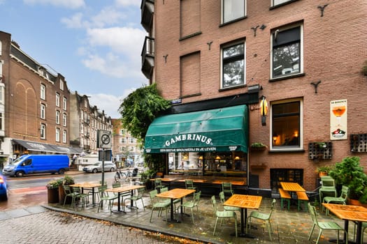 A cozy street cafe featuring wooden tables and green chairs, surrounded by elegant brick buildings under a cloudy sky. Ideal for outdoor dining and relaxation.