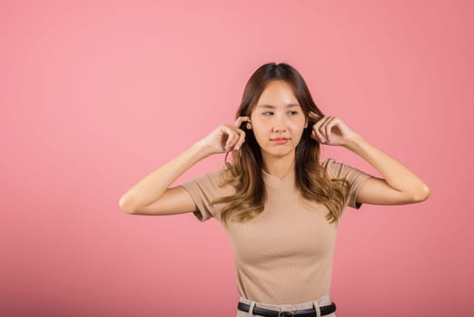 Woman bad mood pain her closed ears with finger and close eyes, Asian beautiful young female covers ears for loud noise, studio shot isolated on pink background with copy space, bad pressure