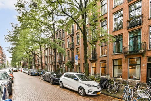 A picturesque urban street showcasing classic Amsterdam architecture, lined with trees, parked cars, and bicycles that capture the essence of city life.