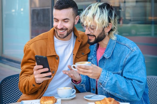 Smiling friends sit together at an outdoor cafe, enjoying coffee and pastries while looking at a smartphone. Relaxed moment of connection, modern lifestyle and social interaction in urban setting.