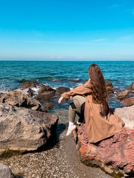 Young caucasian female with long hair relaxing by rocky seaside in casual outfit.