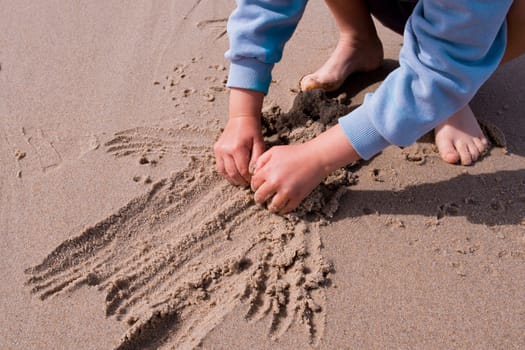 Child playing in sand at beach with hands and feet visible.