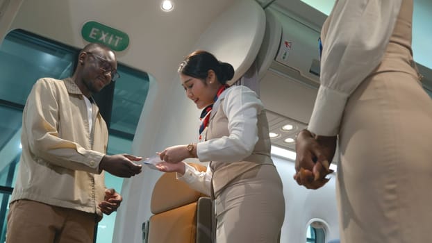 Asian flight attendants greeting welcoming passengers walking and coming on board in airplane, happy air stewardess or airhostess check passenger ticket boarding pass during trip travelling