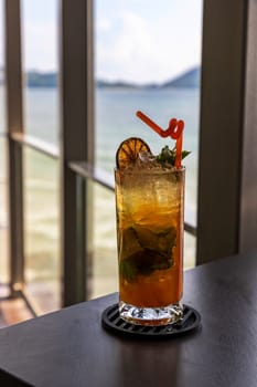 A glass of sweet and refreshing water is placed on a table on a wooden balcony in a restaurant by the sea. the background is the sea The mountain and blue sky are cloudy during the day.Selective focus