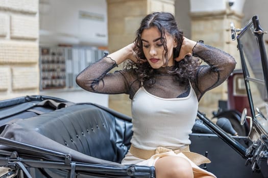 Beautiful long black hair girl is posing on the vintage car looking down. Horizontally.