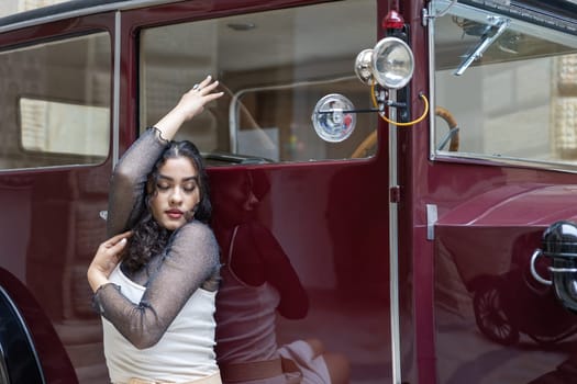 Tanned black hair girl is posing on red vintage car with closed eyes. Horizontally.