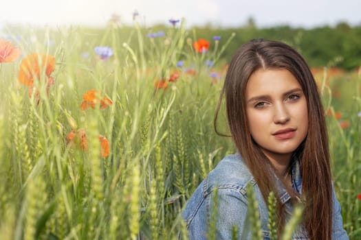Beautiful brunette girl is posing in  cereal field. Red poppies and blue  cornflowers in the sunlight are in the background.