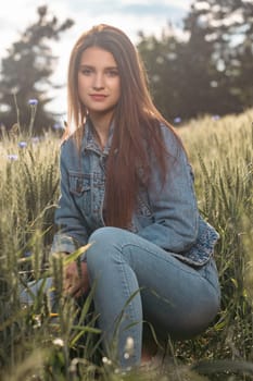 Atractive long haired  brunette girl dressed in jeans is posing in a cereal field. Vertically.