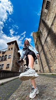 Low-angle urban portrait of a young woman in Girona, Spain, with her sneaker sole in focus against a backdrop of historic buildings. Bold modern travel vibe