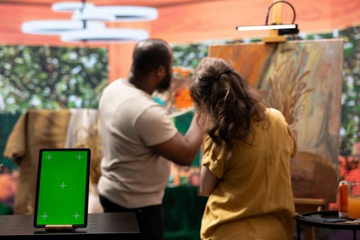 Skilled painters working on an artistic creation next to chroma key screen, using watercolor paint and brush kit to create a masterpiece. Two diverse artists enjoying their creative hobby.