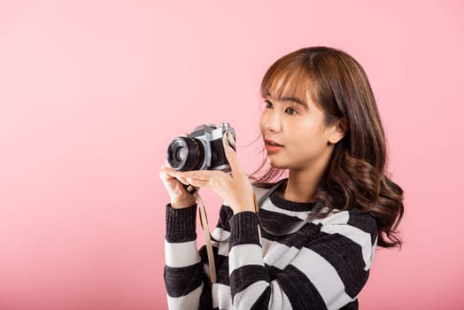 Attractive energetic happy Asian portrait beautiful young woman smiling photographer taking a picture and looking viewfinder on retro vintage photo camera ready to shoot isolated on pink background