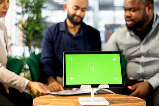 Green screen device next to teamworking colleagues in office coordinating company administrative operation. Close up of mockup tablet used by multiracial coworkers reviewing business data metrics