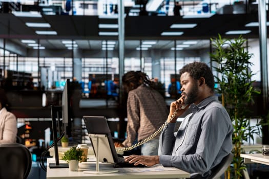 African american investor on a landline phone call negotiating funds at his desk, managing an expansion project and discussing growth strategies. CEO multitasking for a career success.