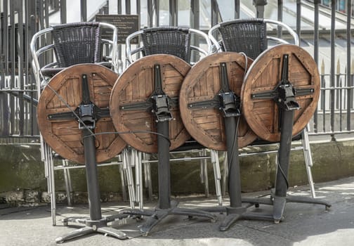 Newcastle, UK - Apr 13, 2025 - Wooden tables and Stainless steel chairs piled up along the Iron fence next to the walkway front of Pub & Restaurant. use it as your Wallpaper, Poster and Space for text, Selective focus.