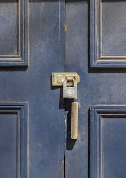 Newcastle, UK - Apr 13, 2025 - Silver colour locked padlock in Brass door lock hasp latch on the blue painted wooden door frame. Storage security, use it as your Wallpaper, Poster and Space for text, Selective focus.