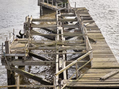 Newcastle, UK - Apr 11, 2025 - A broken of wooden supports of old timber jetty next to Swing bridge or Swing span bridge spanning the River Tyne. Crumbling pier over river, use it as your Wallpaper, Poster and Space for text, Selective focus.
