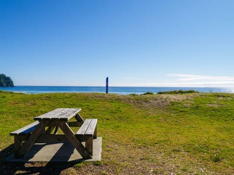 Grassy dune and outdoor table in view of ocean-beach to distant horizon at Mount Maunganui.