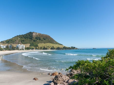 Landmark Mount Maunganui at end of long sandy beach under blue sky Tauranga New Zealand.
