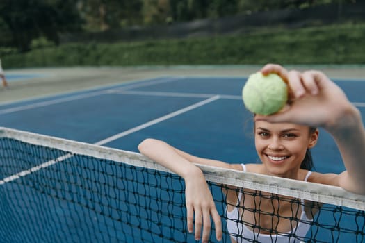 Happy young female tennis player at the net, holding a tennis ball and smiling, representing joy in sports, fitness, and athleticism, perfect for promotional materials