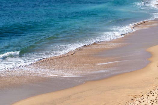Soft beautiful ocean wave gently rolling onto sandy beach. Turquoise sea stretches out, creating a peaceful and serene coastal view