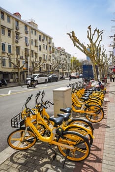 Shanghai, China - 1 April 2025: Yellow bike parking in Pudong. Road, pedestrians, old house, cars. Spring day