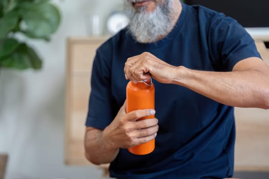 An elderly man opening a water bottle at home, promoting hydration and wellness in his daily life while enjoying a peaceful atmosphere.