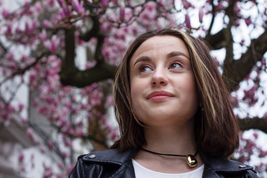 Portrait of a pretty young brunette woman with brown eyes under blooming pink magnolia flowers. High quality photo