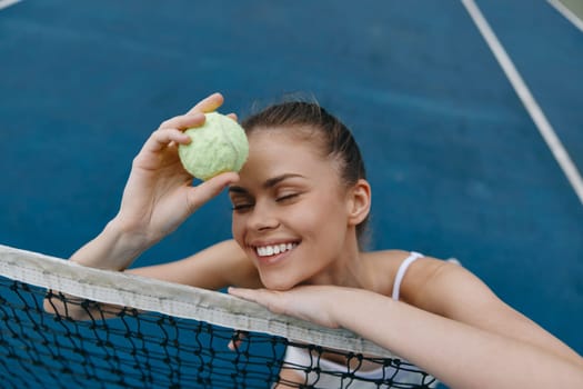 Joyful young woman with a tennis ball, expressing excitement on a blue tennis court, reflecting her passion for the sport and a healthy lifestyle