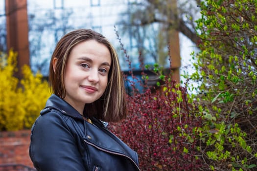 Girl in a black jacket near ornamental bushes in spring. High quality photo